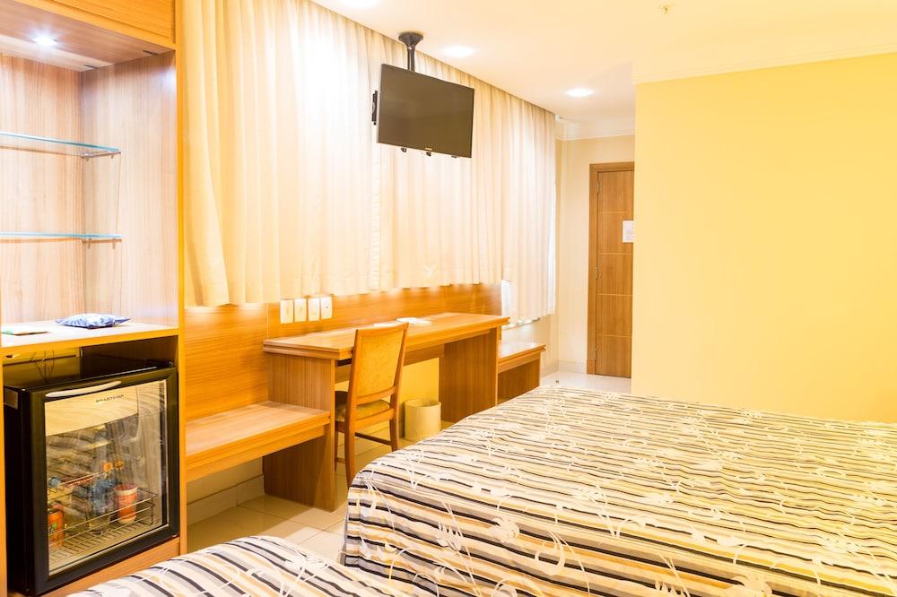 Hotel Atlantico Business Centro ริโอเดจาเนโร ภายนอก รูปภาพ The photo shows a hotel room with two beds featuring striped bedding. There is a wooden desk and chair near a window with light-colored curtains. A flat-screen television is mounted on the wall, and there appears to be a small refrigerator or mini-ba