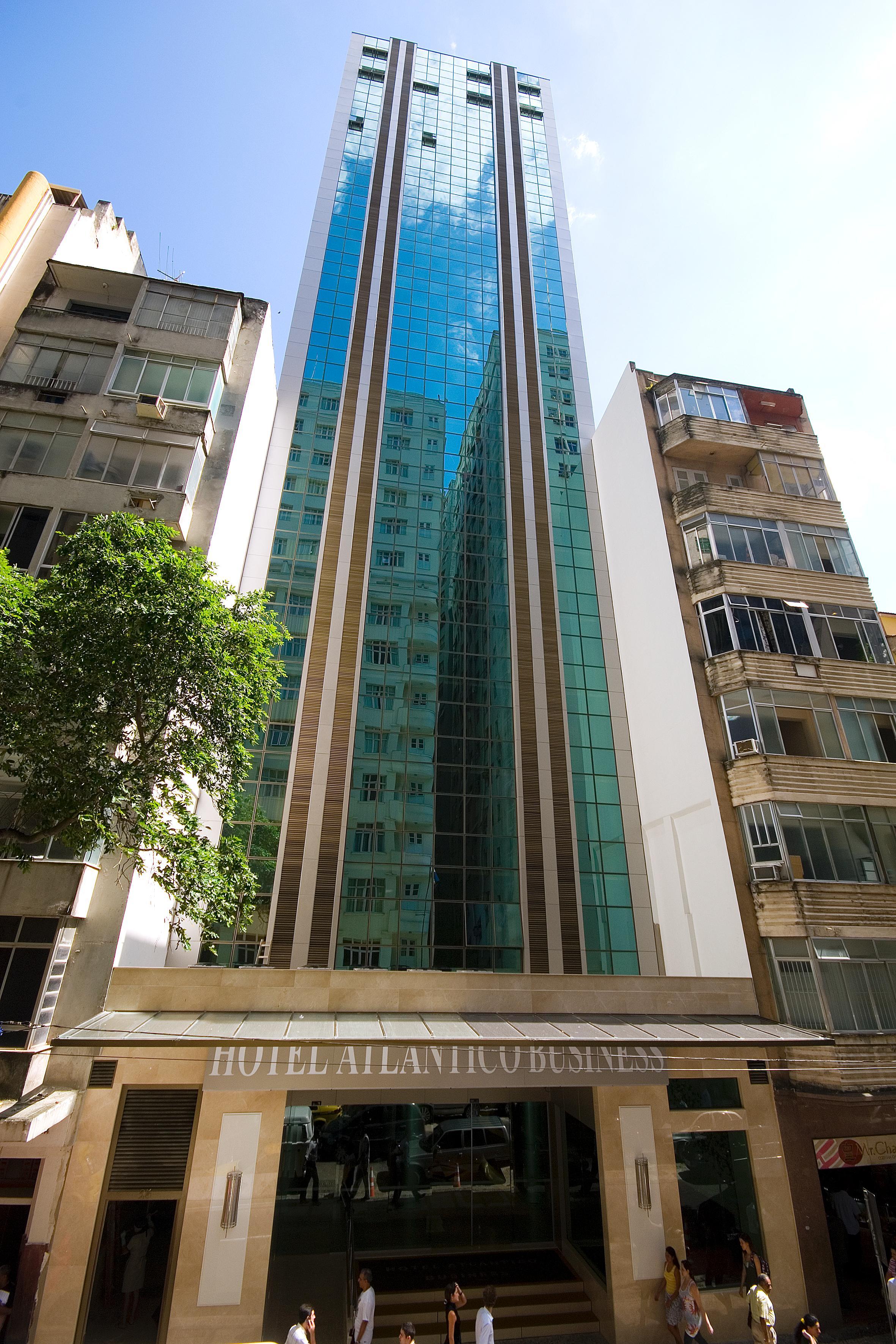 Hotel Atlantico Business Centro ริโอเดจาเนโร ภายนอก รูปภาพ The photo shows a modern multi-story building with a sleek glass facade. The building appears to have several floors with large windows, reflecting sunlight, and is flanked by a tree on one side and an older, more traditional residential structure on